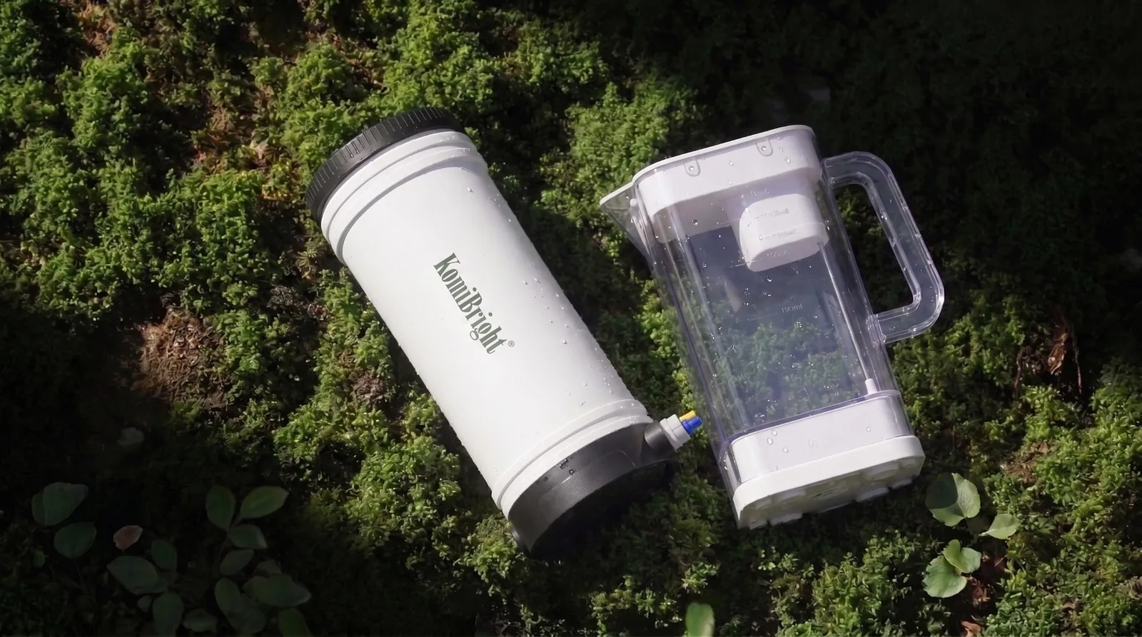 A KomiBright RO body and a ZenJar lying side by side on a bed of forest moss, beaded with water.